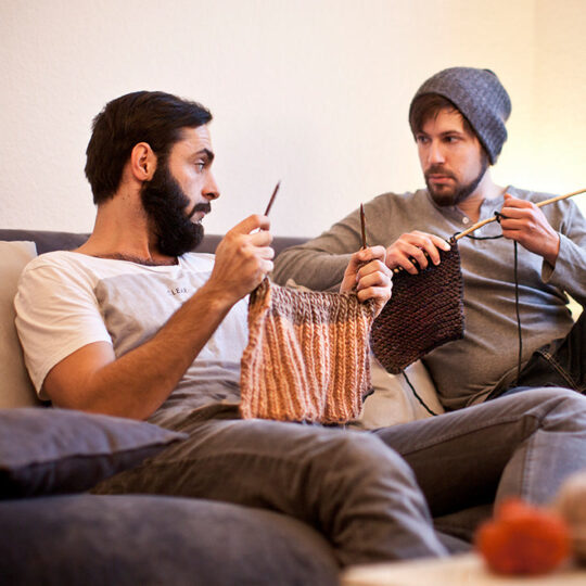 Zwei Männer stricken zusammen.